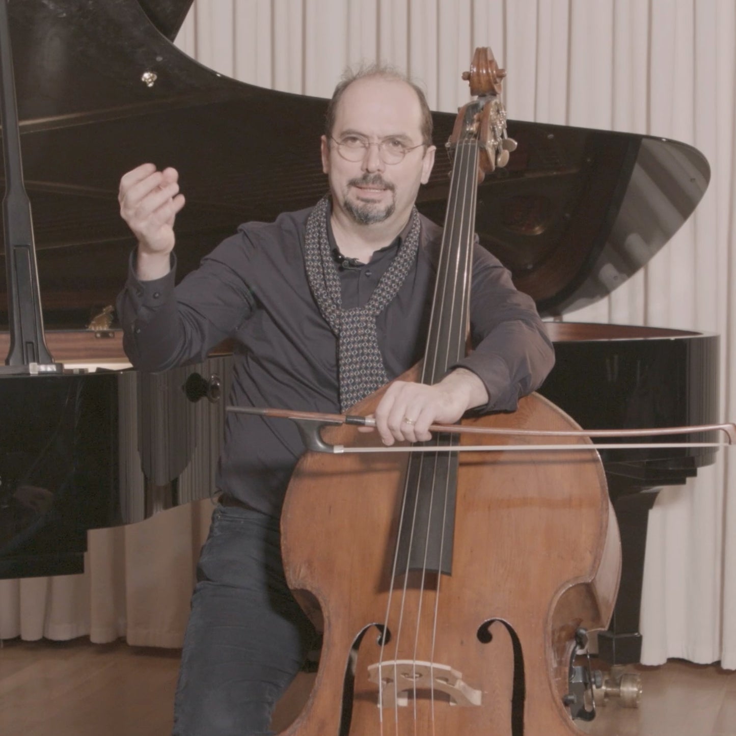 Petru Iuga mid sentence holding a double bass and German double bass bow in a studio.