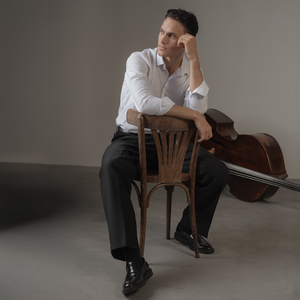 Studio shot of bassist Dmytro Rudyk sat on a chair with a double bass behind him.