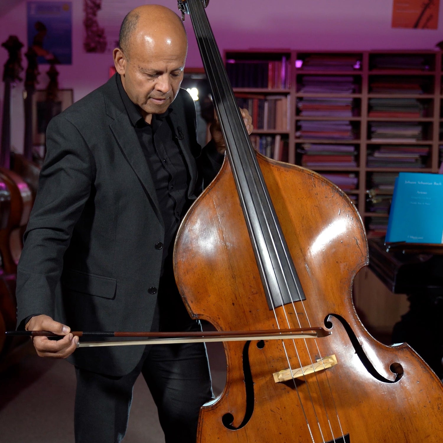 Leon Bosch playing a double bass with a German bow, in front of a bookshelf with various books.