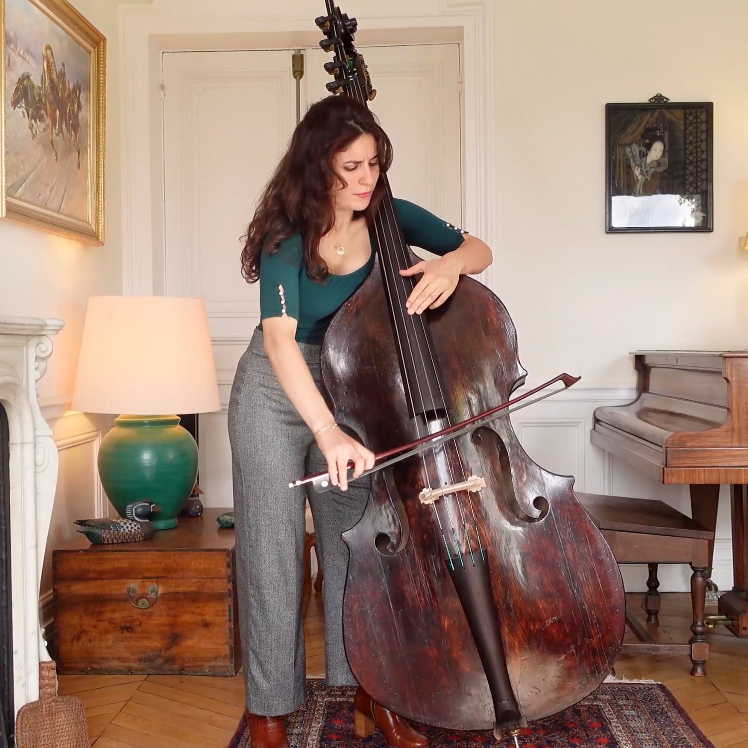 Lorraine Campet playing a double bass  in a room with a piano and various decorations.