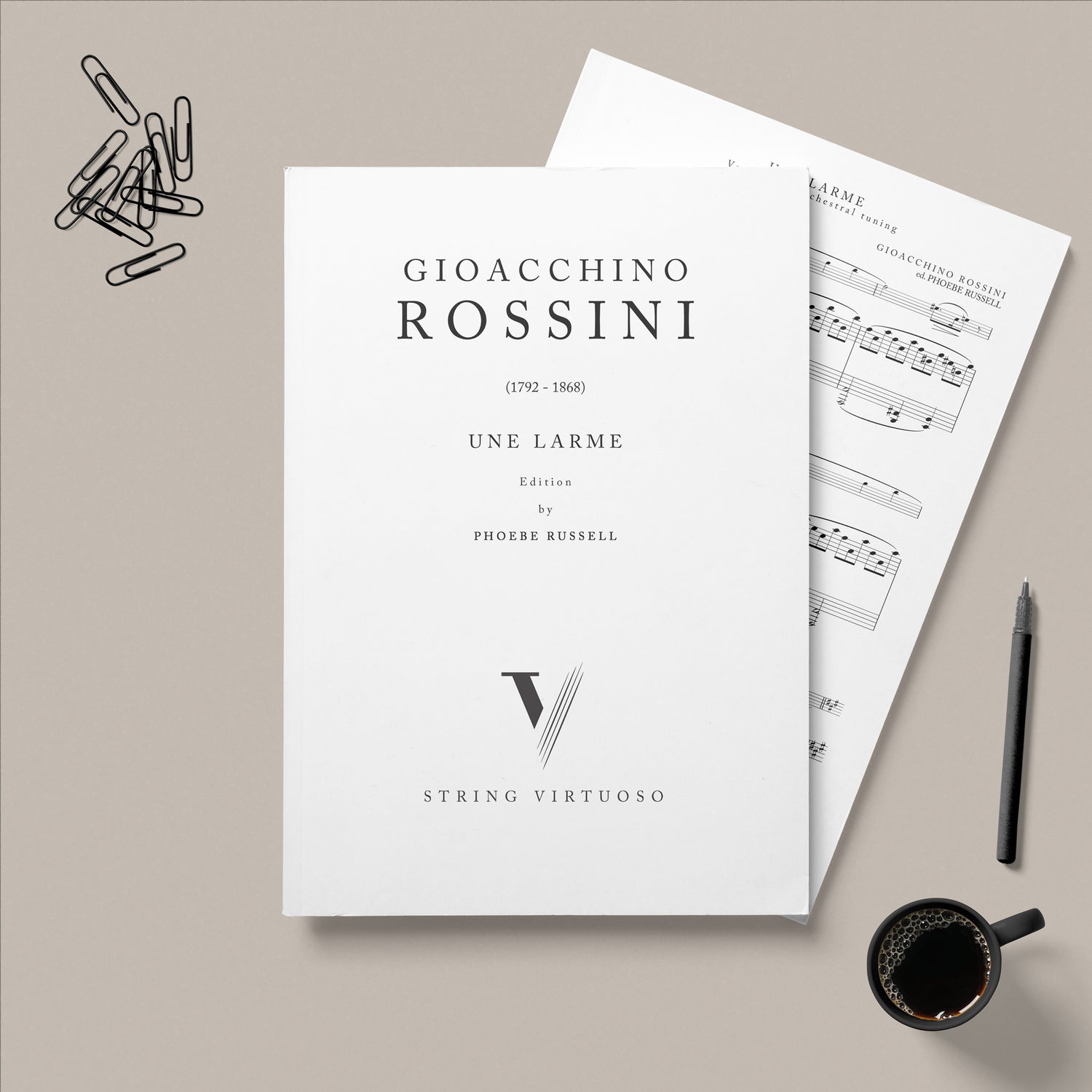 PDF Sheet Music of Gioacchino Rossini's Une Larme edition by Phoebe Russell, laid on a beige background with paper clips, a pen and a cup of coffee.